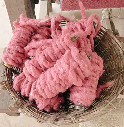 Basket filled with handspun pink Khadi cotton yarn bobbins, prepared for traditional weaving in an Indian textile workshop