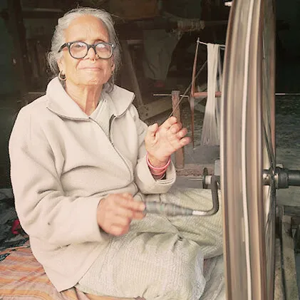 Elderly woman spinning Khadi cotton using a traditional charkha wheel at an Indian handloom center