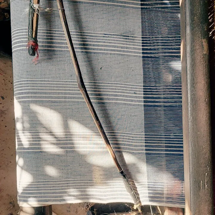 Close-up of blue and white striped Khadi cotton fabric on a handloom with a traditional weaving tool placed on top